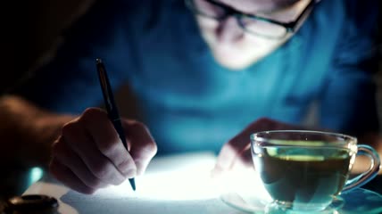 失眠男子拿着一杯茶写字特写实拍