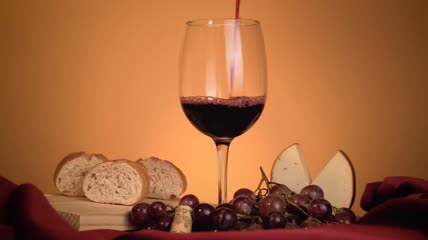 一杯红酒周围有葡萄、面包和奶酪特写