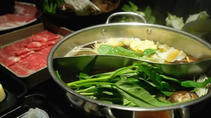 人正在给锅中添加涮菜特写